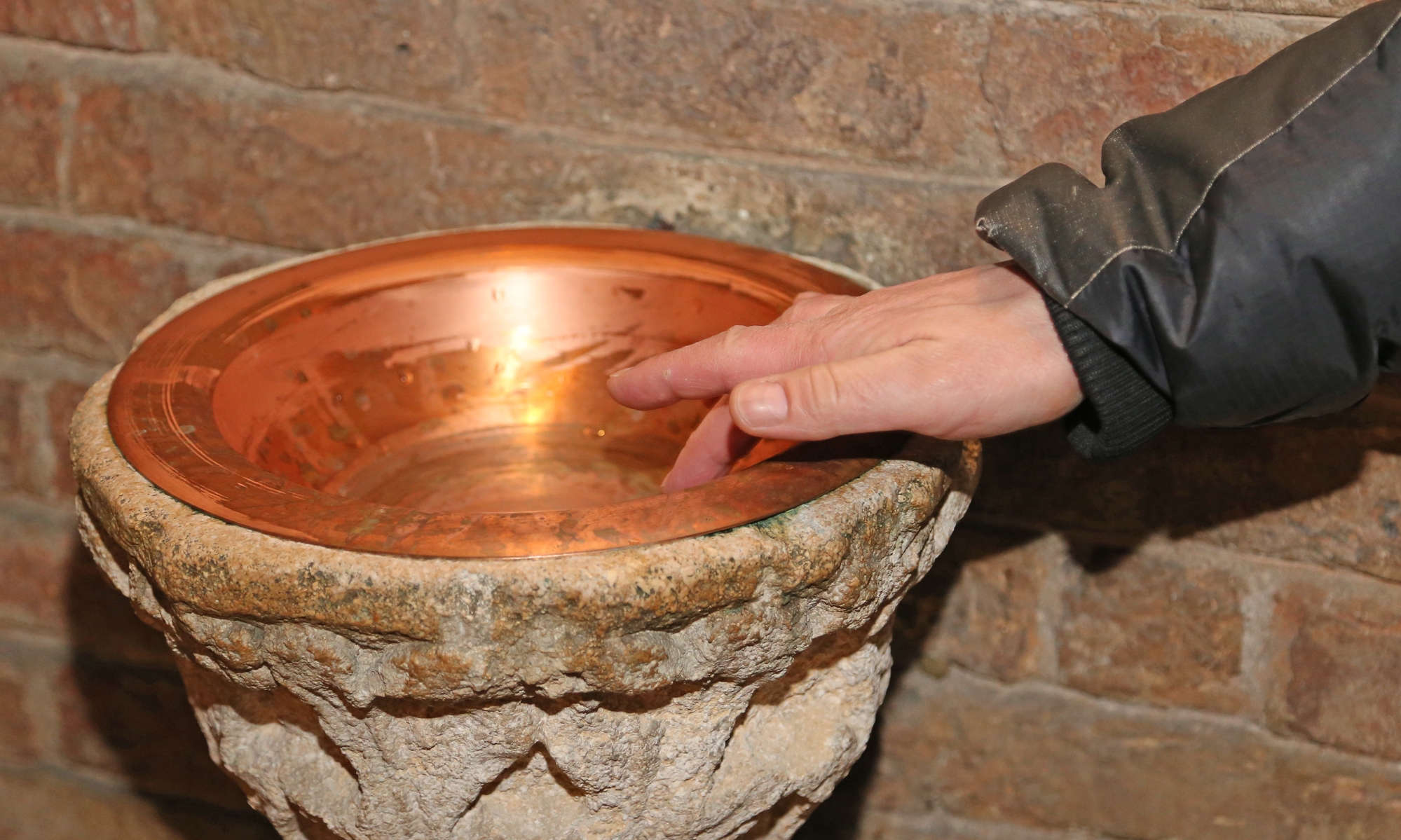 hand of man and an ancient stoup inside the Church
